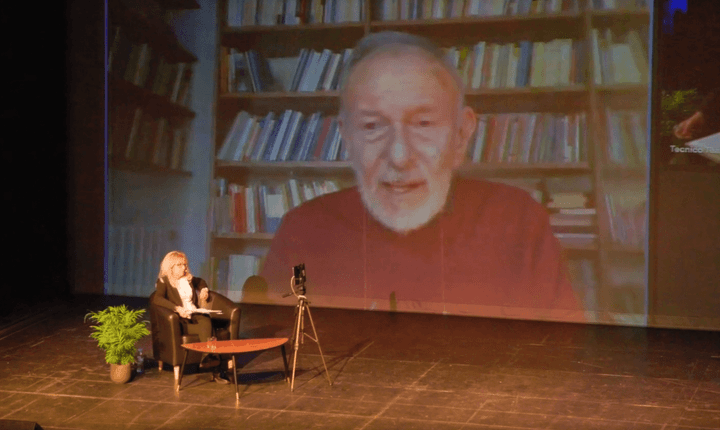 foto di una donna seduta da sola su un palco, che mostra una grande foto di un uomo anziano projecte