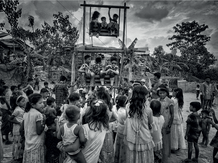 una foto in bianco e nero di decine di bambini attorno a una piccola ruota panoramica di legno