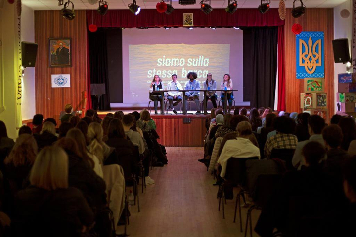 Un auditorium pieno di pubblico che ascolta cinque persone su un palco