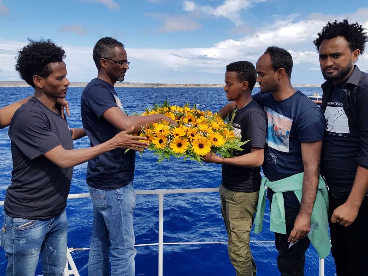 cinque uomini scuri su una barca e una ghirlanda di fiori gialli
